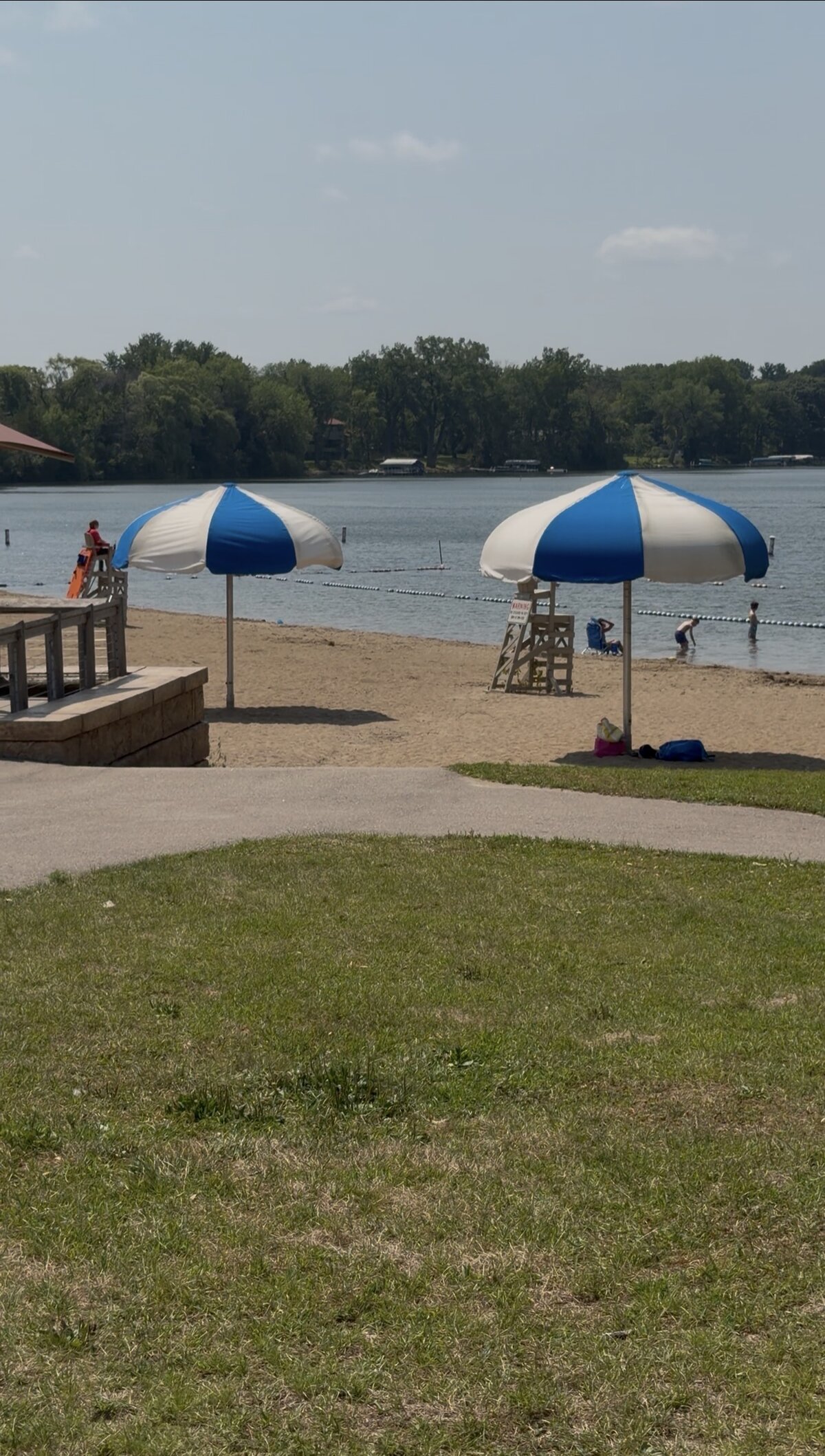 A sandy beach at Riley Lake Park with striped umbrellas and swimmers in the roped-off swim area