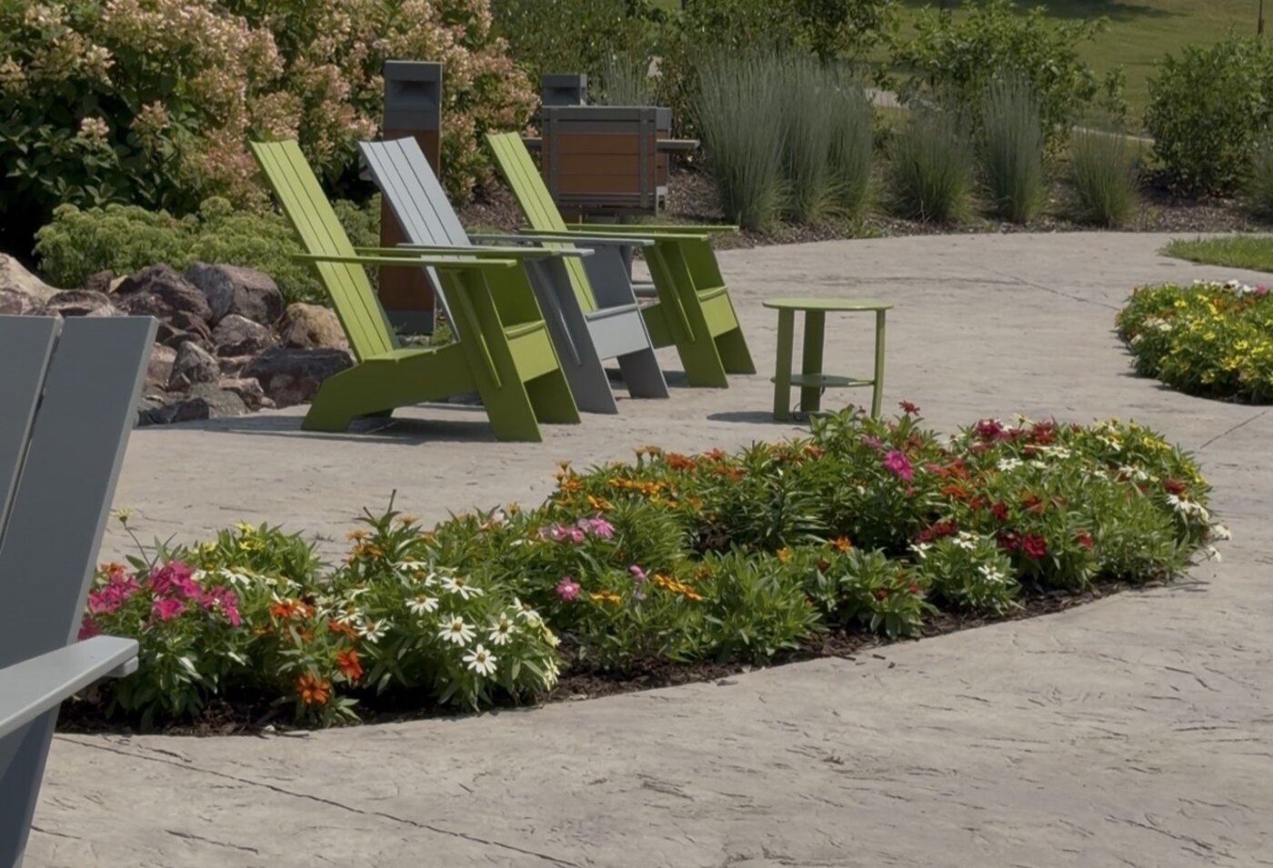 Colorful Adirondack chairs and a small table on a patio surrounded by flower gardens at Riley Lake Park