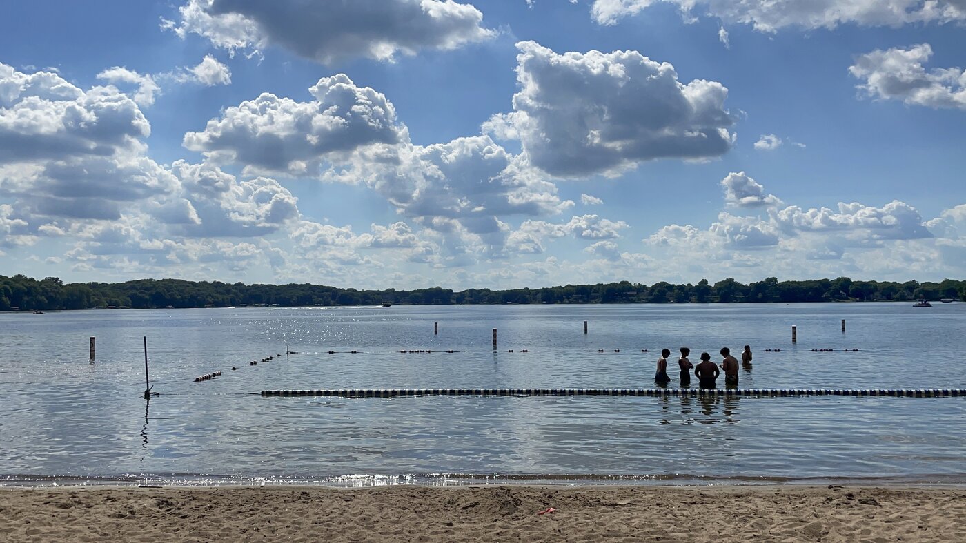 People wading in the clean water of Riley Lake near the roped swim line, with a wide sky overhead